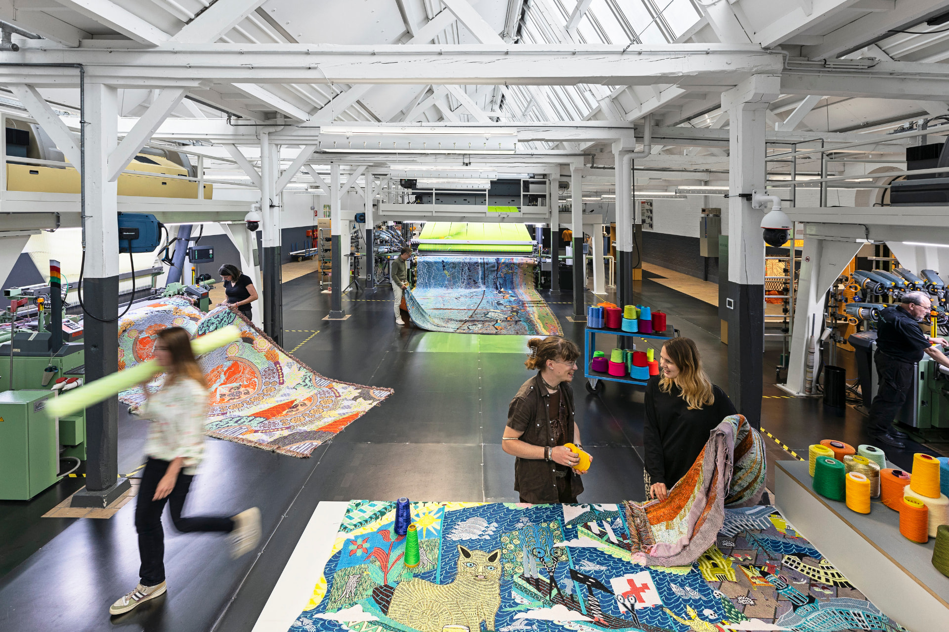 Makers werken tussen textielmachines, garens en kleurrijke stoffen in het TextielMuseum