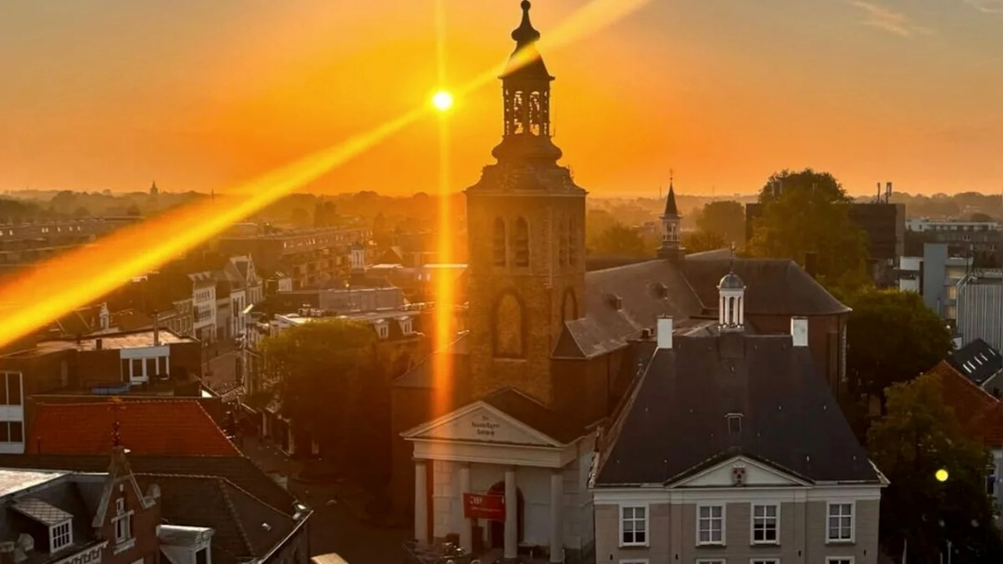 De toren van de Sint Jan de Doperkerk boven de daken van Roosendaal bij zonsopkomst