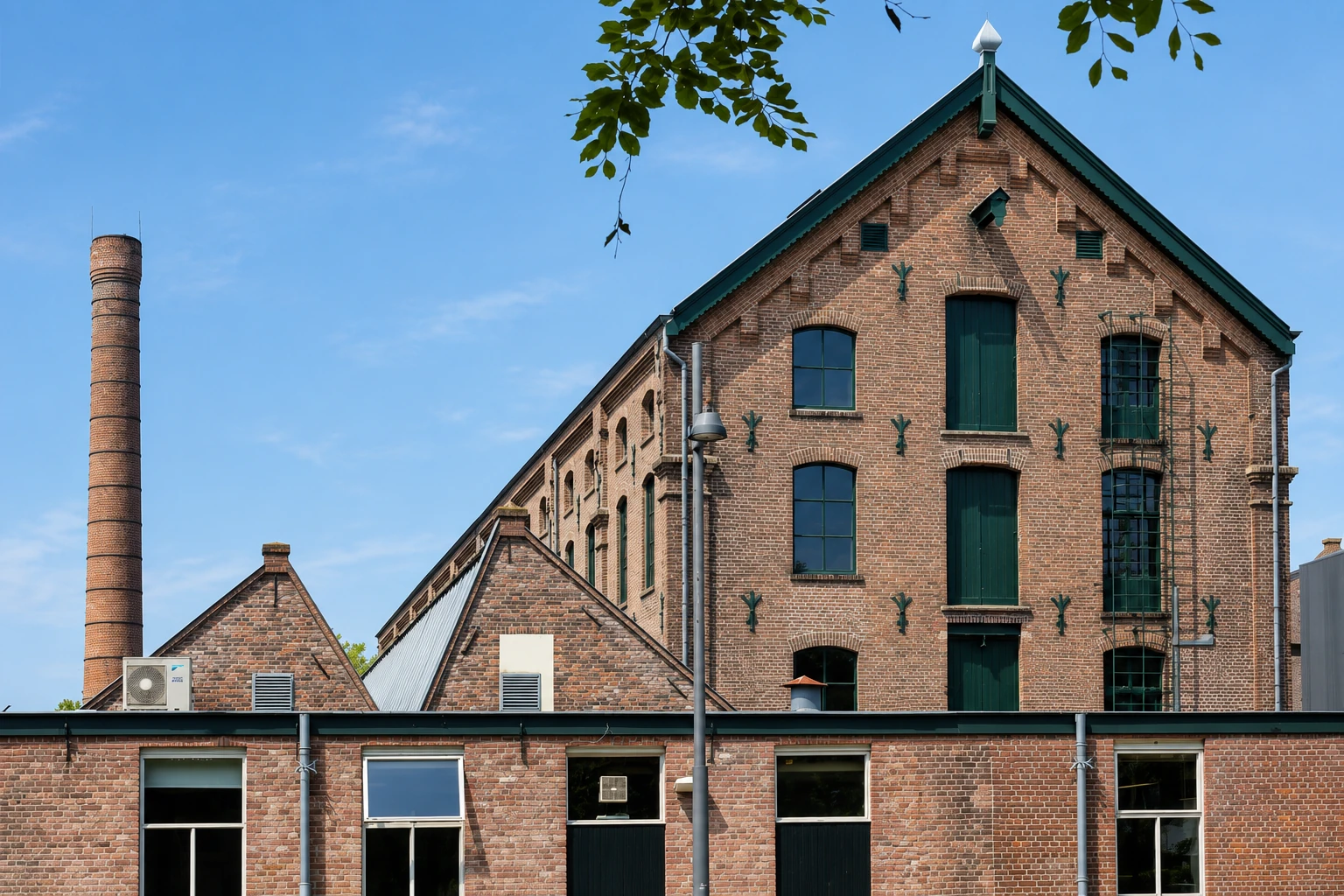 Bakstenen textielfabriek van de TextielCampus in Tilburg met hoge schoorsteen tegen een blauwe lucht